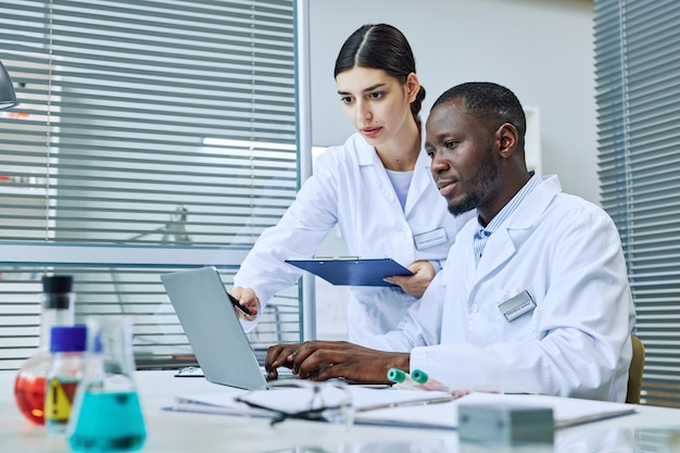 Retrato de dois cientistas usando laptop enquanto fazem pesquisas no espaço de cópia de laboratório médico