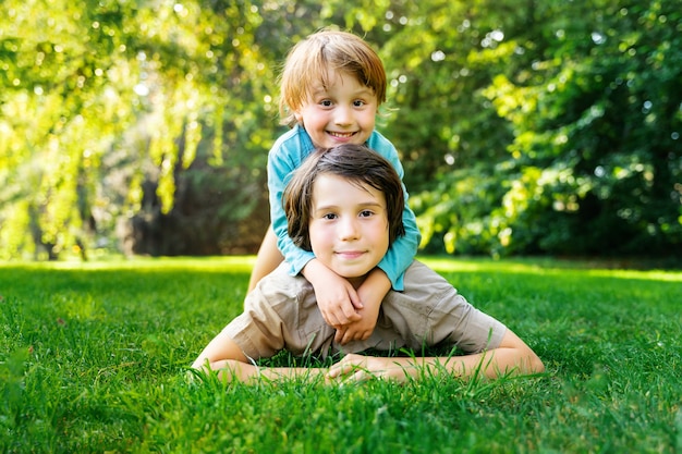 Retrato de dois irmãos, deitado em uma grama e brincando juntos em um parque ao pôr do sol. sorrindo crianças felizes ao ar livre. amizade de irmãos.