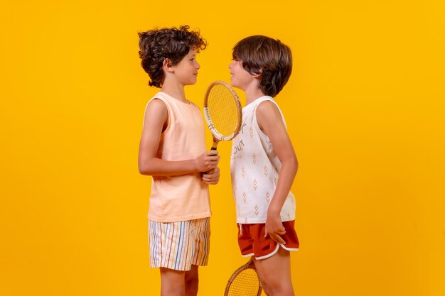 Retrato de dois irmãos jogando tênis e se divertindo nas férias de verão fundo amarelo