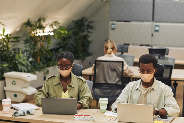 Retrato de dois jovens afro-americanos usando máscaras enquanto trabalhava em um escritório pós-pandêmico, copie o espaço