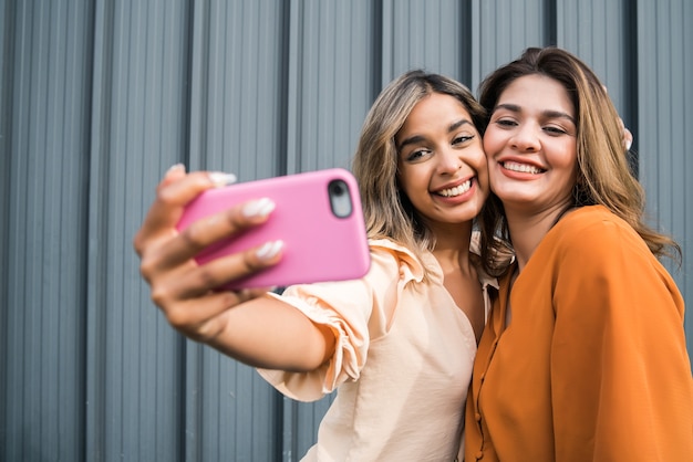 Retrato de dois jovens amigos se divertindo juntos e tirando uma selfie com um telefone celular ao ar livre. conceito urbano.