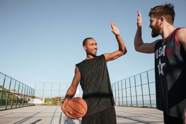 Retrato de dois jovens desportistas dando high five enquanto jogava basquete no parquinho