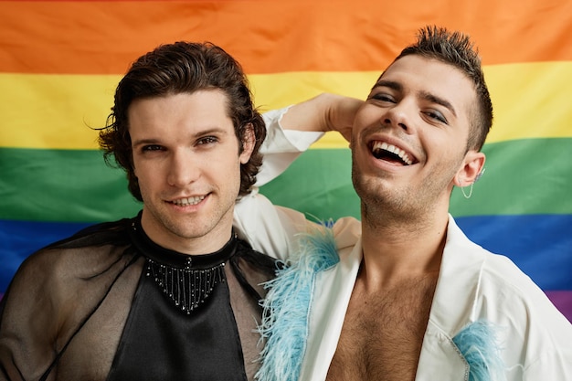 Retrato de dois jovens gays posando com a bandeira do orgulho lgbtq ao fundo e rindo despreocupados