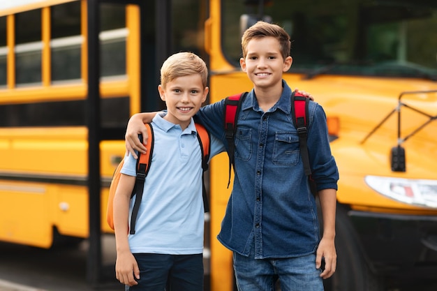 Retrato de dois meninos felizes posando ao ar livre perto do ônibus escolar