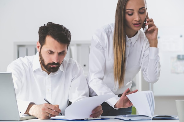 Foto retrato de dois parceiros de negócios. ambos estão vestindo camisas brancas e trabalhando juntos em seu escritório. ela está ao telefone. ele está escrevendo.