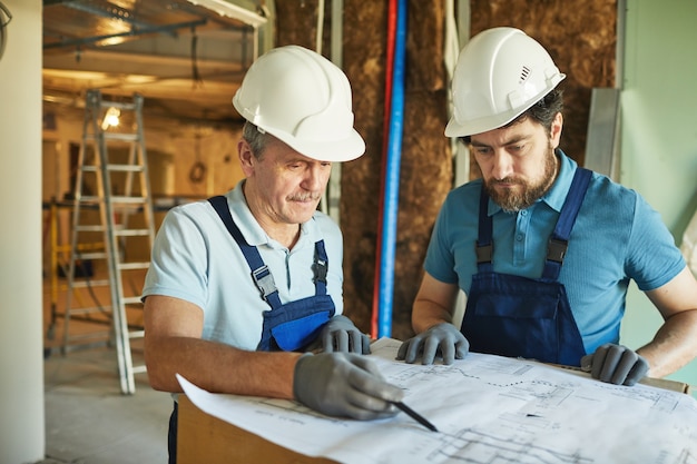 Retrato de dois trabalhadores da construção civil usando capacetes de proteção enquanto olha para as plantas enquanto reforma a casa, copie o espaço