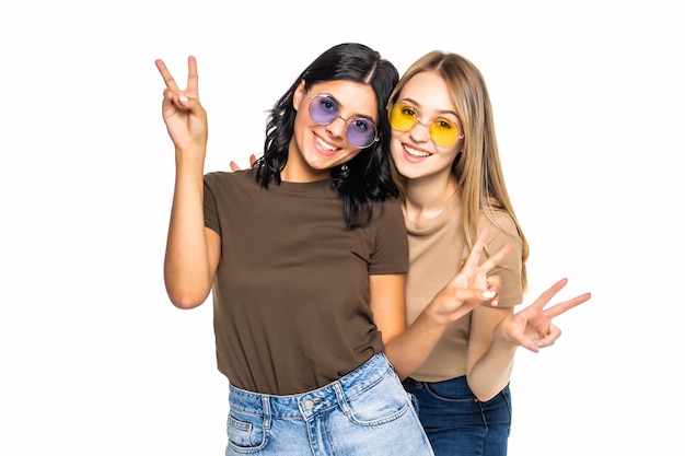 Foto retrato de duas amigas mostrando sinal de dois dedos na parede cinza e olhando para a frente