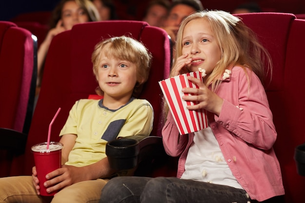 Retrato de duas crianças assustadas assistindo filme no cinema e comendo pipoca, copie o espaço