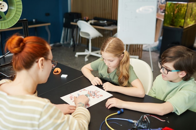 Retrato de duas crianças olhando esquemas e planos durante a aula de engenharia e robótica na escola moderna, copie o espaço