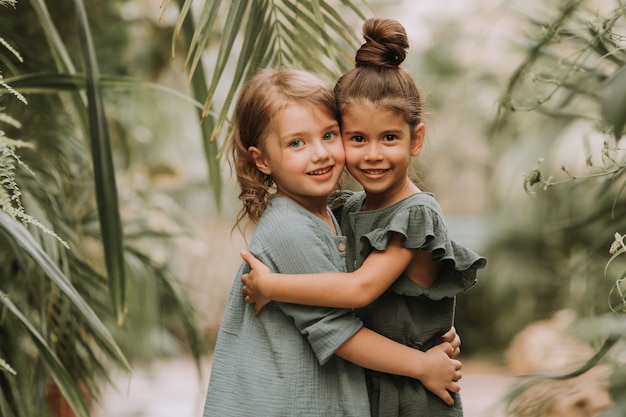 Retrato de duas encantadoras garotas sorridentes pertencentes a diferentes raças cercadas por folhas tropicais