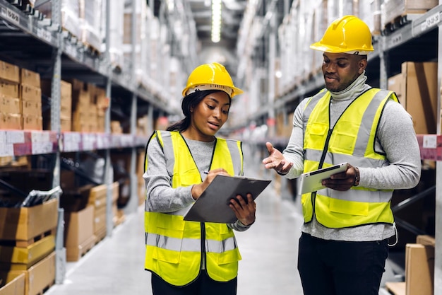 Retrato de duas equipes de engenheiros afro-americanos, detalhes do pedido de remessa no tablet, verifique mercadorias e suprimentos nas prateleiras com estoque de mercadorias na indústria de logística de armazém de fábrica e exportação de negócios