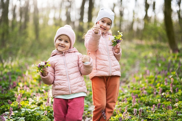 Retrato de duas irmãzinhas com buquê de flores na floresta ensolarada Conceito de lazer de primavera ao ar livre