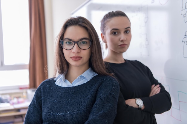 retrato de duas jovens estudantes em frente a uma lousa branca e olhando para a câmera