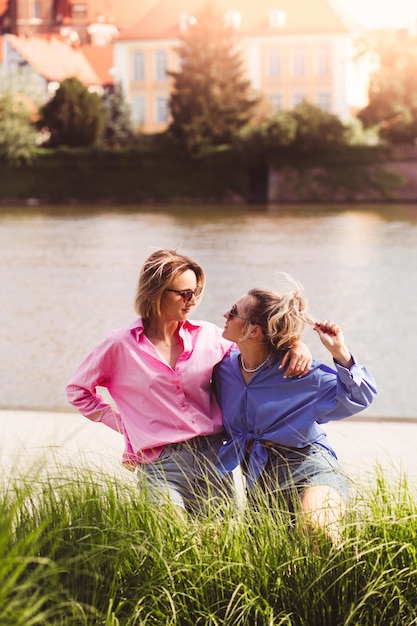 Retrato de duas jovens lindas e sorridentes hipster femininas em roupas de cores de verão na moda mulheres despreocupadas posando no fundo do rio Modelos positivos se divertindo abraçando