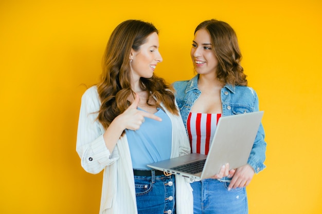 Retrato de duas jovens negras chocadas apontando o dedo para o computador portátil em amarelo