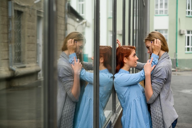Retrato de duas lésbicas em pé na rua e tocando-se suavemente LGBT jovem casal gay feminino A garota pressiona apaixonadamente seu parceiro de vida contra a parede do espelho