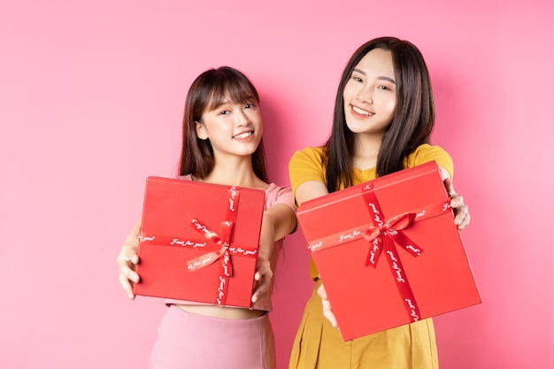 Retrato de duas lindas garotas asiáticas segurando uma caixa de presente vermelha em uma parede rosa