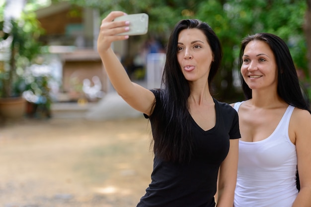 Retrato de duas lindas mulheres felizes tirando uma selfie juntas ao ar livre