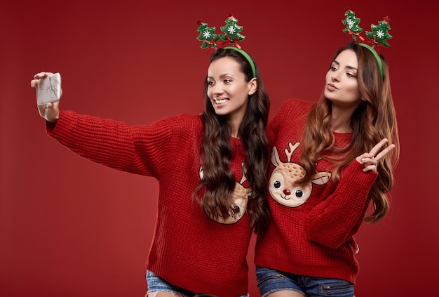 Retrato de duas melhores amigas malucas em um suéter aconchegante de inverno com atributos de Natal tomando selfie