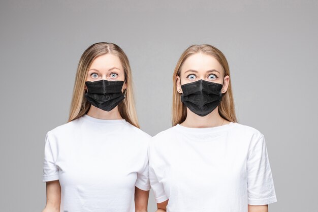 Retrato de duas meninas bonitas com cabelo longo loiro com máscaras médicas negras em seus rostos isolados
