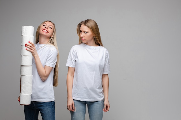 Retrato de duas meninas bonitas com cabelo longo loiro, um deles tem um monte de papel higiênico e outro é ofendido isolado