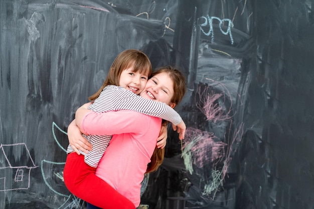 retrato de duas meninas bonitinhas felizes se abraçando enquanto se divertem na frente do quadro negro