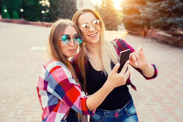 Retrato de duas meninas sorridentes felizes fazendo fotos de selfie no ambiente urbano do smartphone à noite