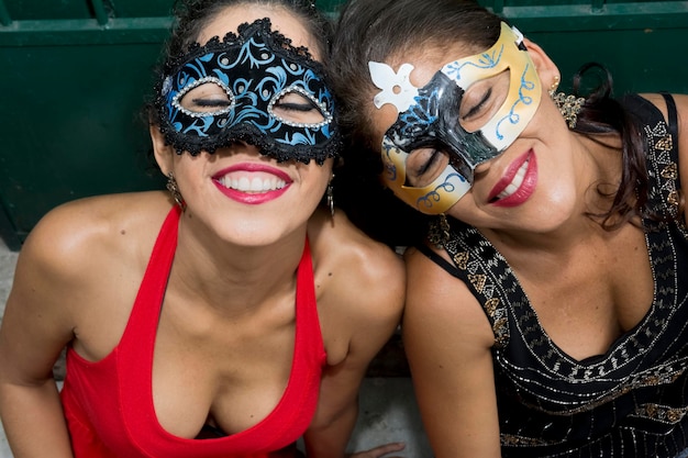 Foto retrato de duas mulheres usando máscara de carnaval sentadas contra uma velha porta histórica