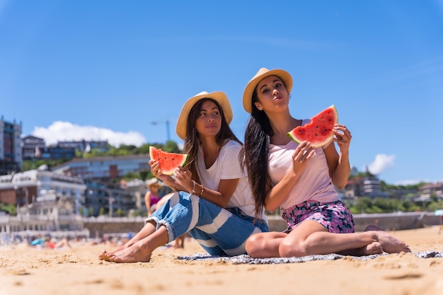 Retrato de duas namoradas no verão na praia comendo uma melancia aproveitando as férias