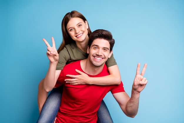 Retrato de duas pessoas casadas positivas relaxam descanso no feriado de 14 de fevereiro homem abraço nas costas sua namorada fazer v-sinais usar camiseta vermelha verde isolada sobre fundo de cor azul