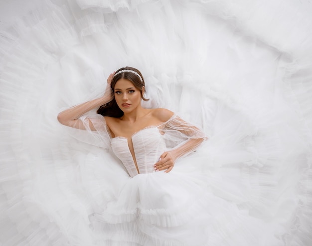 Retrato de elegante jovem caucasiana deitada no lindo vestido de noiva com ombros abertos modelo de noiva atraente posando com maquiagem perfeita para festa de casamento vestido elegante