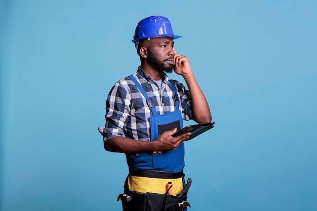 Foto retrato de empreiteiro afro-americano com tablet digital calculando custos e quantidade de materiais necessários para realizar a reforma. supervisor usando aplicativo de estimativa em dispositivo eletrônico.