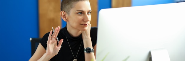 Retrato de empresária adorável falando na vídeo chamada. Computador moderno com símbolo. Encantadora dama acenando Olá. Conceito on-line de tecnologia e reunião de negócios