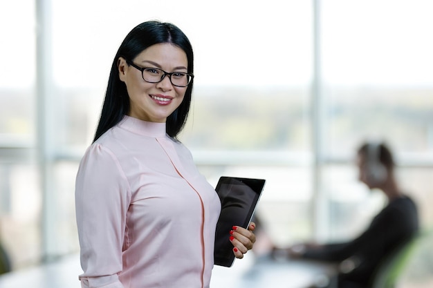 Retrato de empresária asiática segurando o tablet pc fundo desfocado do escritório interno