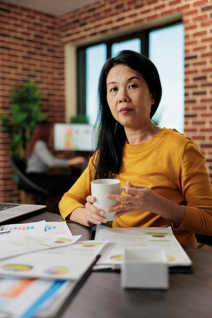 Retrato de empresária asiática sentada à mesa no escritório de inicialização trabalhando no projeto de gerenciamento analisando estatísticas da empresa. Mulher empreendedora, brainstorming de ideias, planejamento de parceria de negócios