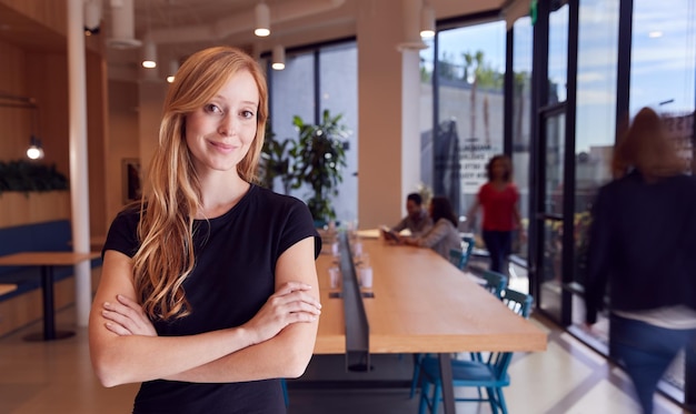 Retrato de empresária de pé no escritório de plano aberto moderno ocupado com colegas em segundo plano