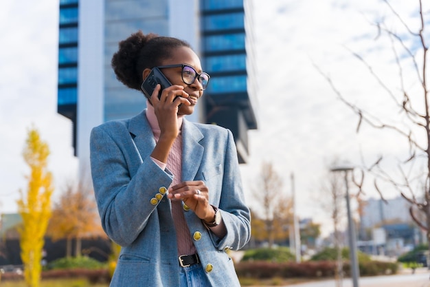 Retrato de empresária étnica negra usando óculos em um parque empresarial sorrindo falando ao telefone