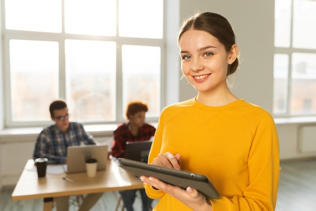 Retrato de empresária líder de equipe feminina em pé no escritório com colegas reunidos em segundo plano