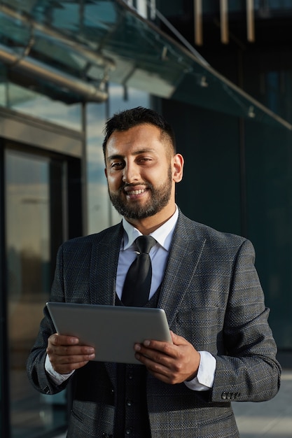 Foto retrato de empresário barbudo em um terno elegante, sorrindo para a câmera enquanto usa o tablet pc ao ar livre