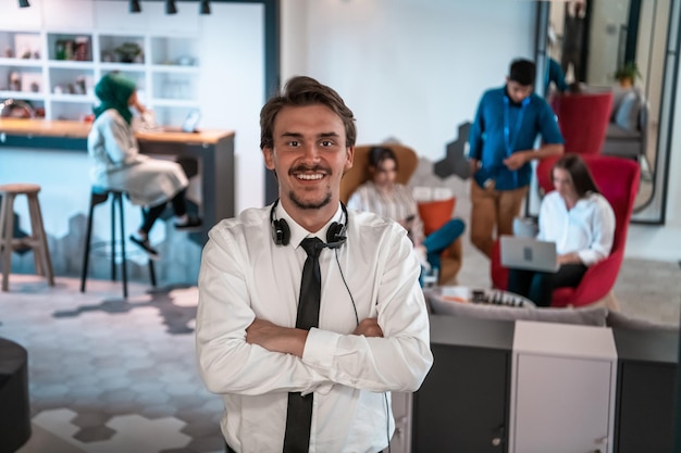 Retrato de empresário bem sucedido empresário com fones de ouvido em volta do pescoço e colegas em segundo plano no escritório de inicialização ocupado. Foto de alta qualidade