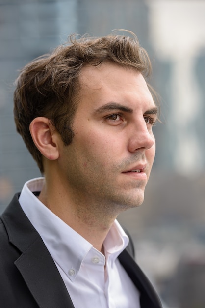 Retrato de empresário com cabelo castanho e terno contra a vista da cidade