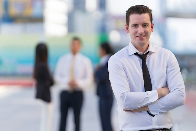 Retrato de empresário de sucesso em pé com os braços cruzados em frente a prédios de escritórios