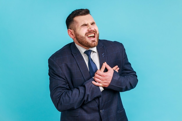 Retrato de empresário doente vestindo terno estilo oficial tendo ataque cardíaco súbito ou cólicas dolorosas problemas cardíacos que sofrem de dor Foto de estúdio interior isolada em fundo azul