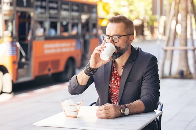 Retrato de empresário feliz de meia-idade bebendo um café ao ar livre