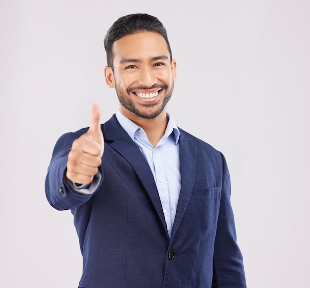 Retrato de empresário feliz e polegares para cima para aprovação de sucesso ou vitória contra um fundo de estúdio cinza Sorriso de homem asiático com emoji sim sinal ou bom trabalho para acordo comercial e obrigado