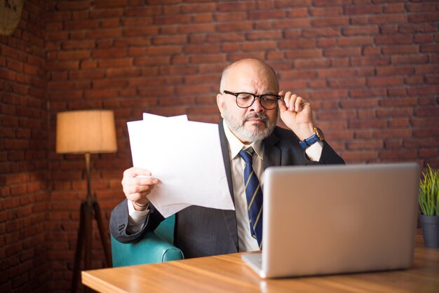 Retrato de empresário indiano asiático jogando ou lendo documentos enquanto está sentado na mesa com o laptop