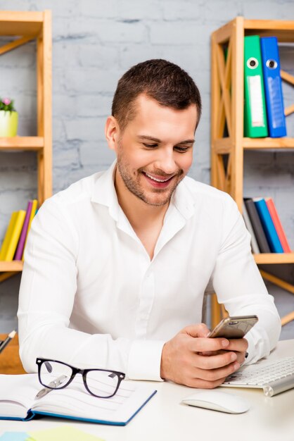 Retrato de empresário sorridente digitando mensagem em seu escritório