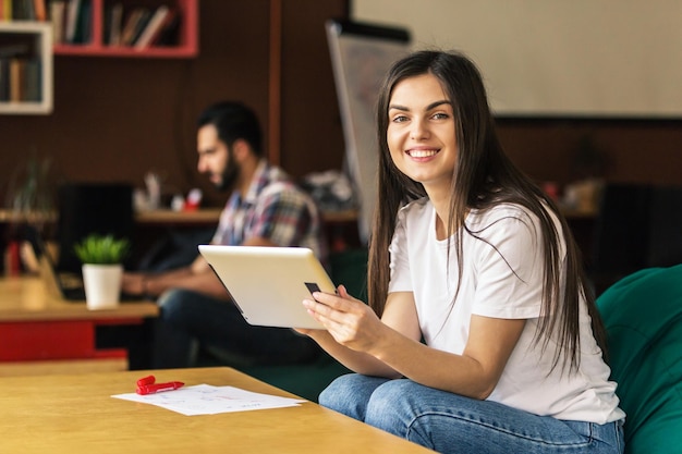 Retrato de empresário sorridente menina morena trabalha com tablet no escritório moderno sentado perto da mesa