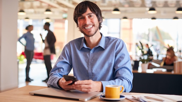 Retrato de empresário sorridente sentado na mesa com laptop no escritório moderno de plano aberto