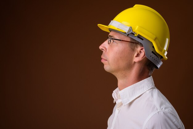 Retrato de empresário usando capacete de segurança contra uma parede marrom